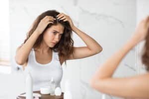 Woman looking in the mirror discovering female pattern hair loss with a look of concern