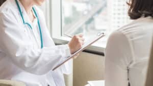 Dermatologst with clipboard going over year-end insurance details with a patient.